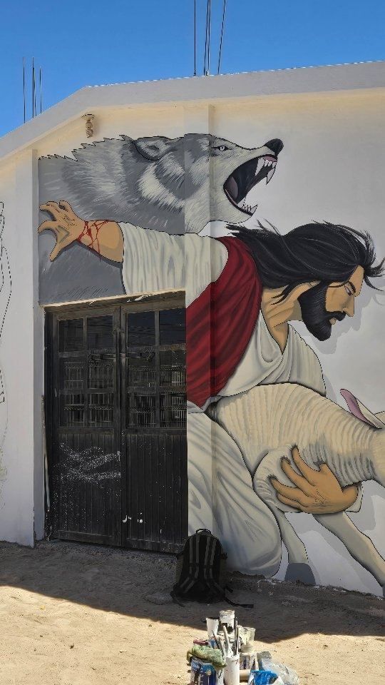 Hand-painted mural of Christ carrying a lamb on a church exterior wall