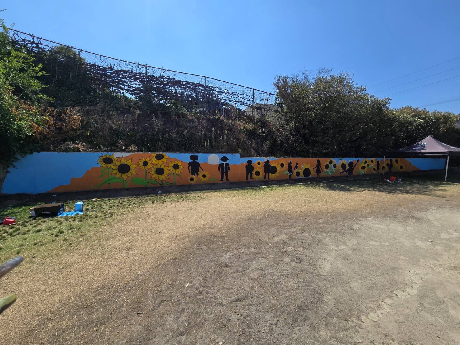 Long wall mural of sunflowers and silhouettes of children on orange and blue