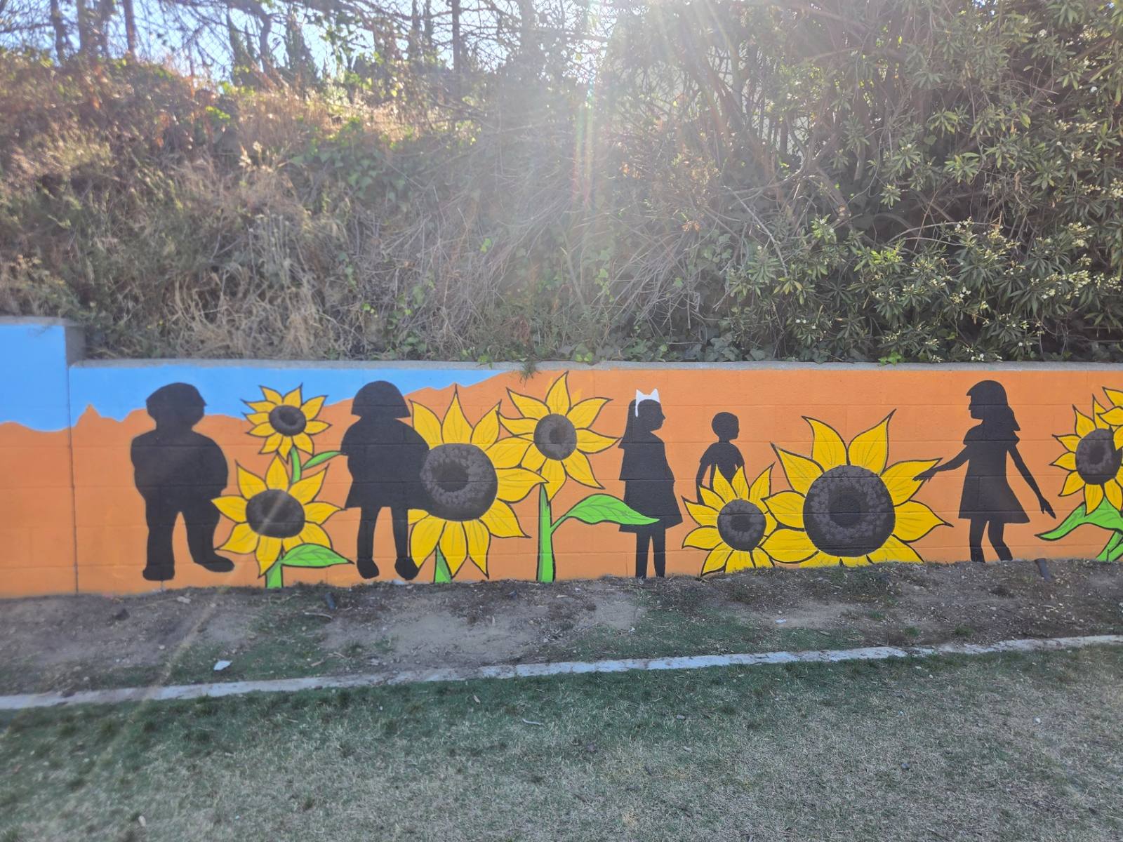 Close view of painted sunflowers and black child silhouettes on an orange wall
