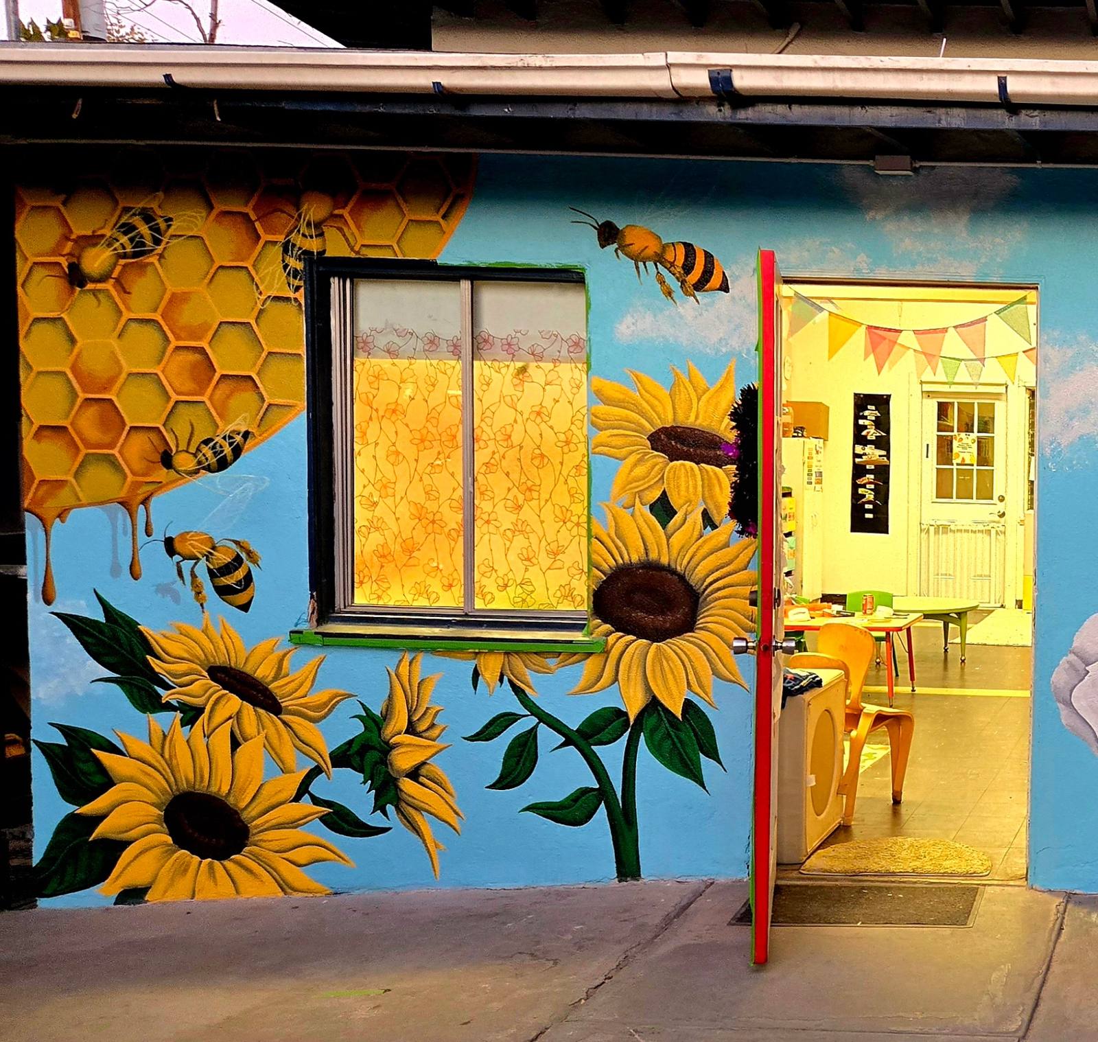 School wall painted with honeycomb, bees and large sunflowers on sky blue