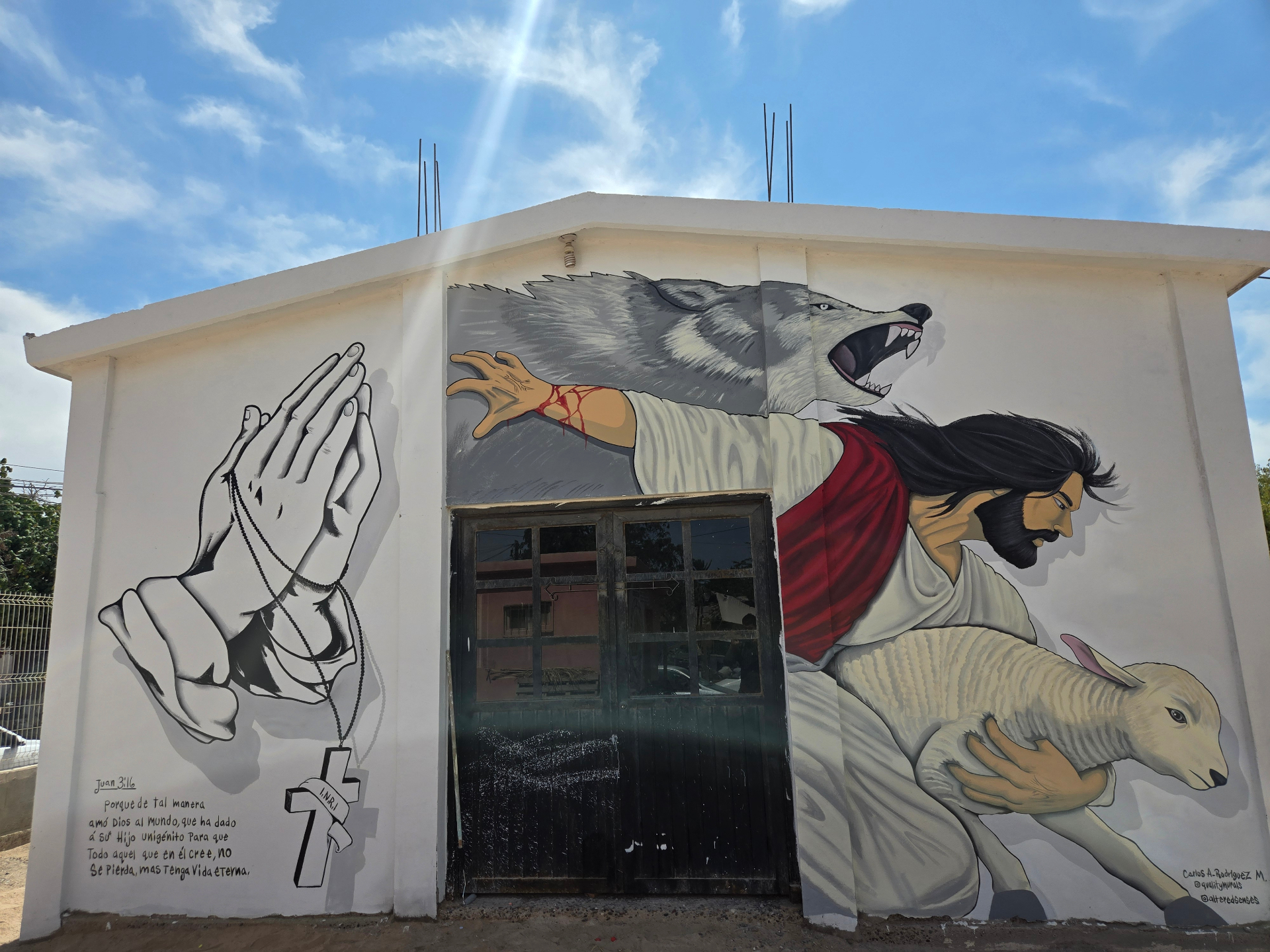 Hand-painted mural of Jesus as the Good Shepherd with a wolf, praying hands, lamb, and John 3:16 on a sanctuary exterior